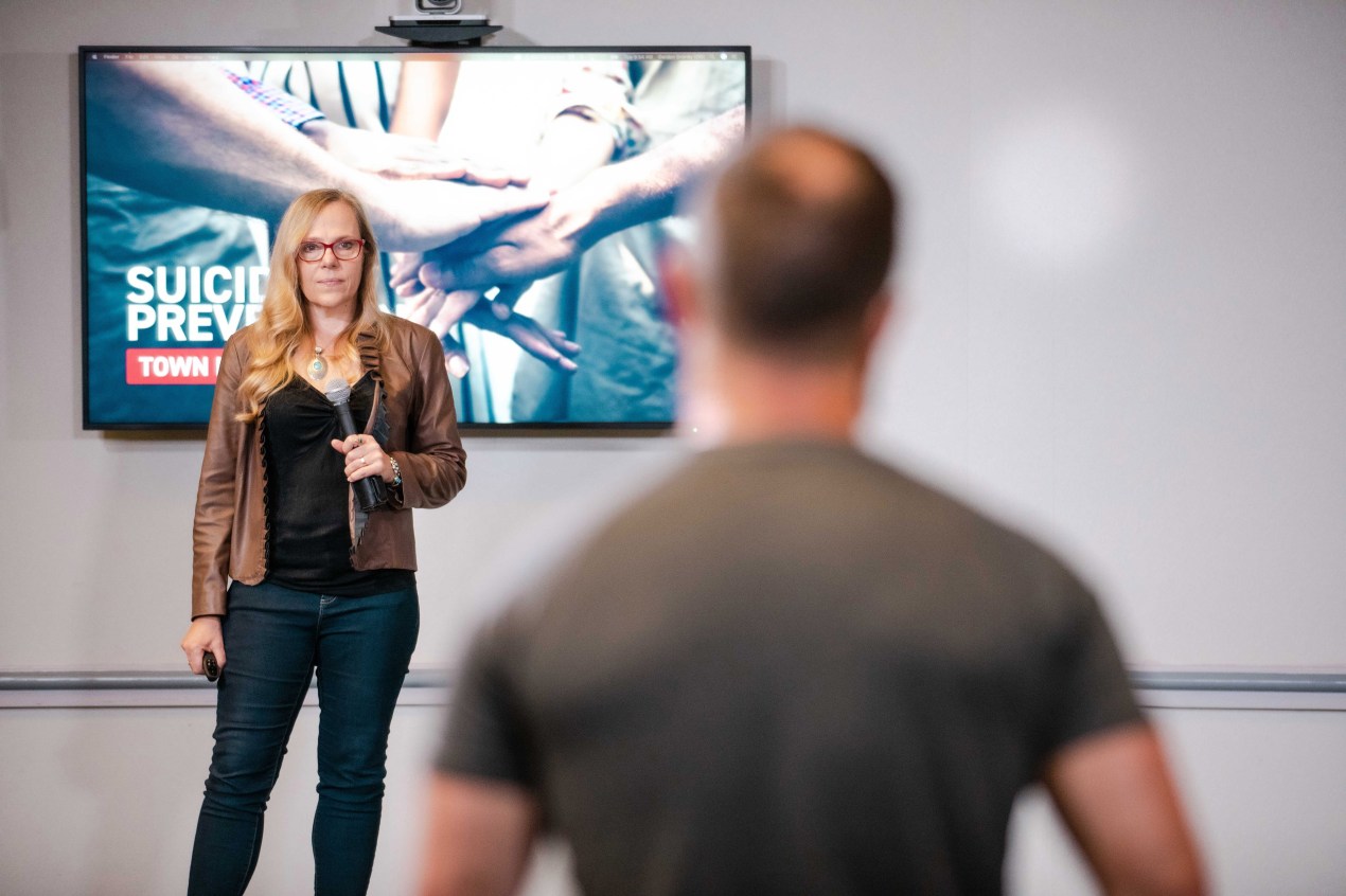 A woman wearing red glasses stands in front of a screen as she holds a microphone.