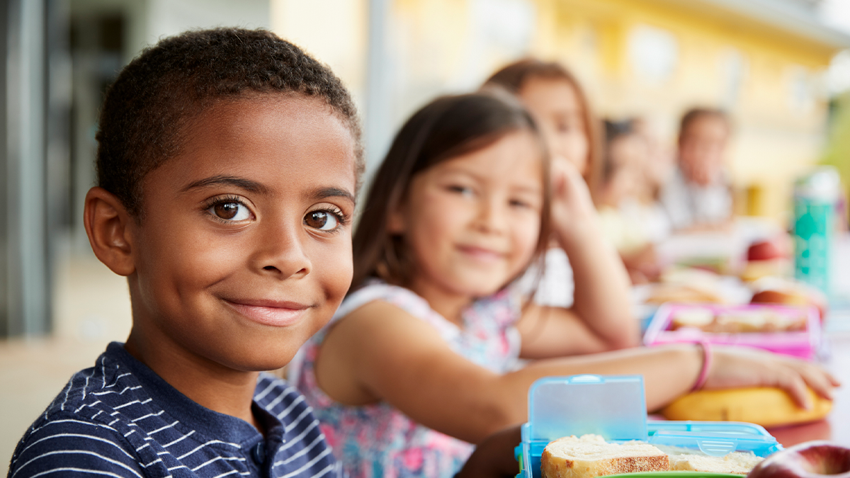 Young boy and girl at school lunch table smiling to camera.