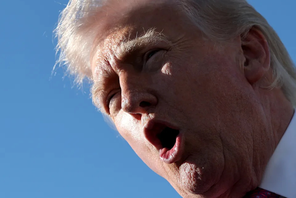 A person speaking outdoors with an open mouth, captured from a low angle against a clear sky