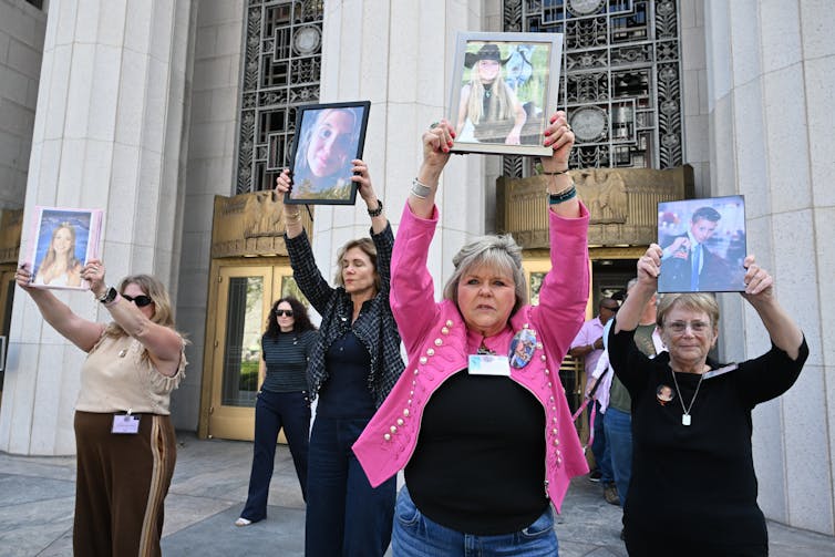 Mothers hold framed photos of their children over their heads outside the courthouse.