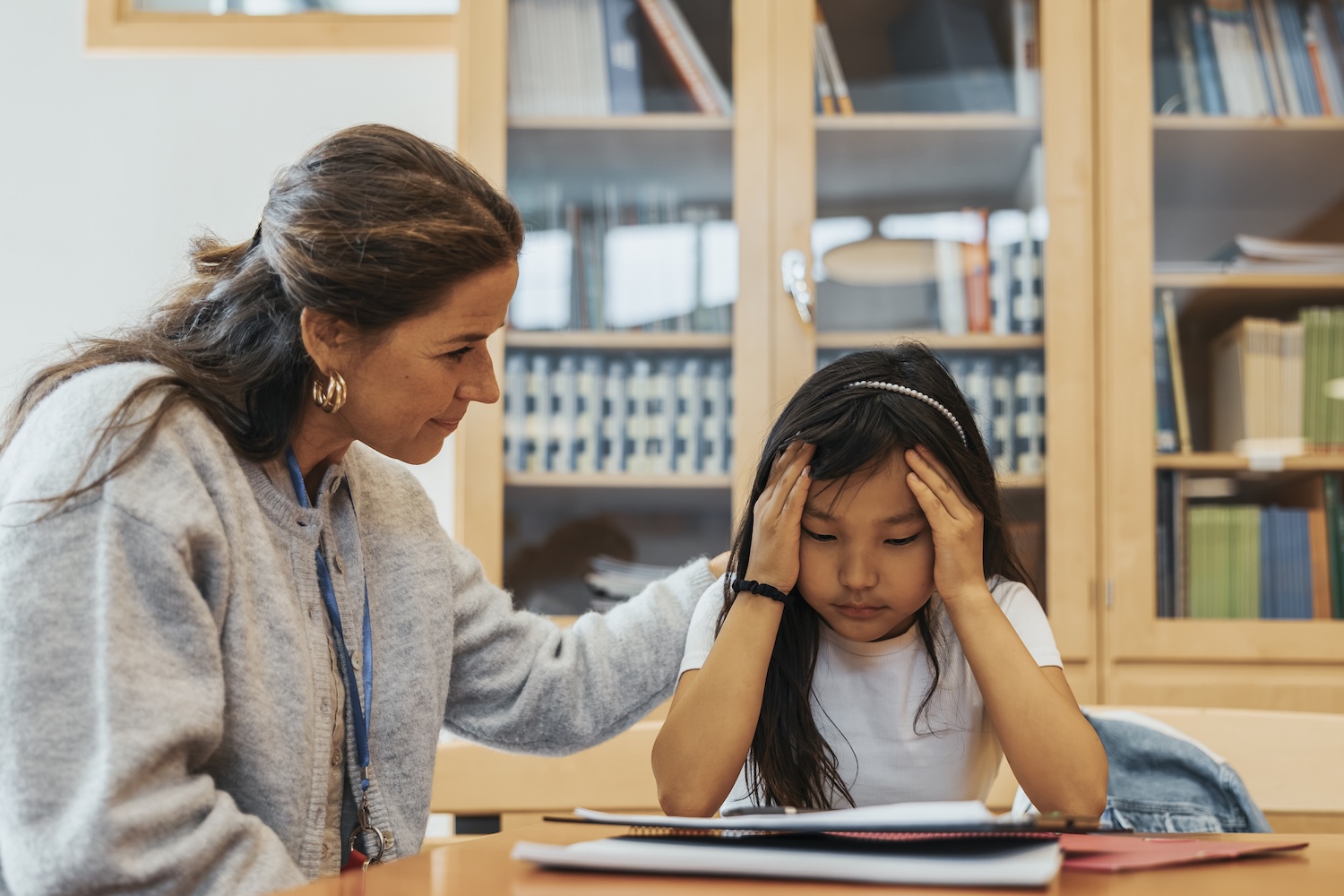 Female counselor consoling girl sitting with head in hands at elementary school