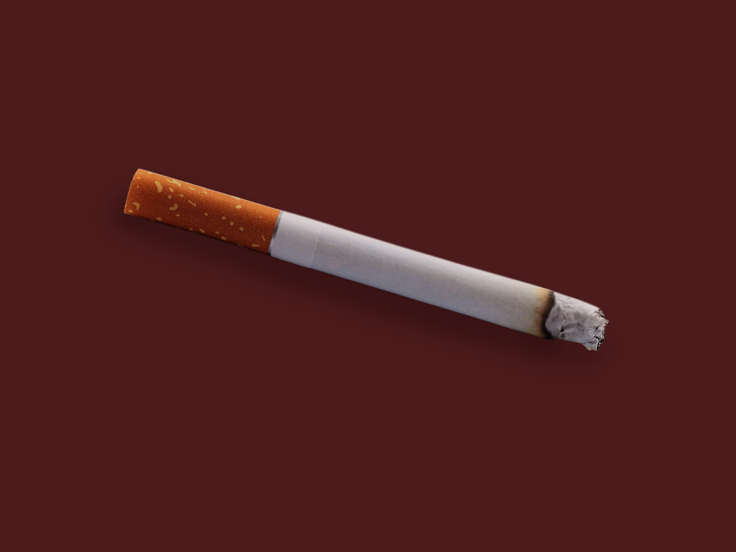 A cigarette pointing downwards, laid on top of a maroon background.