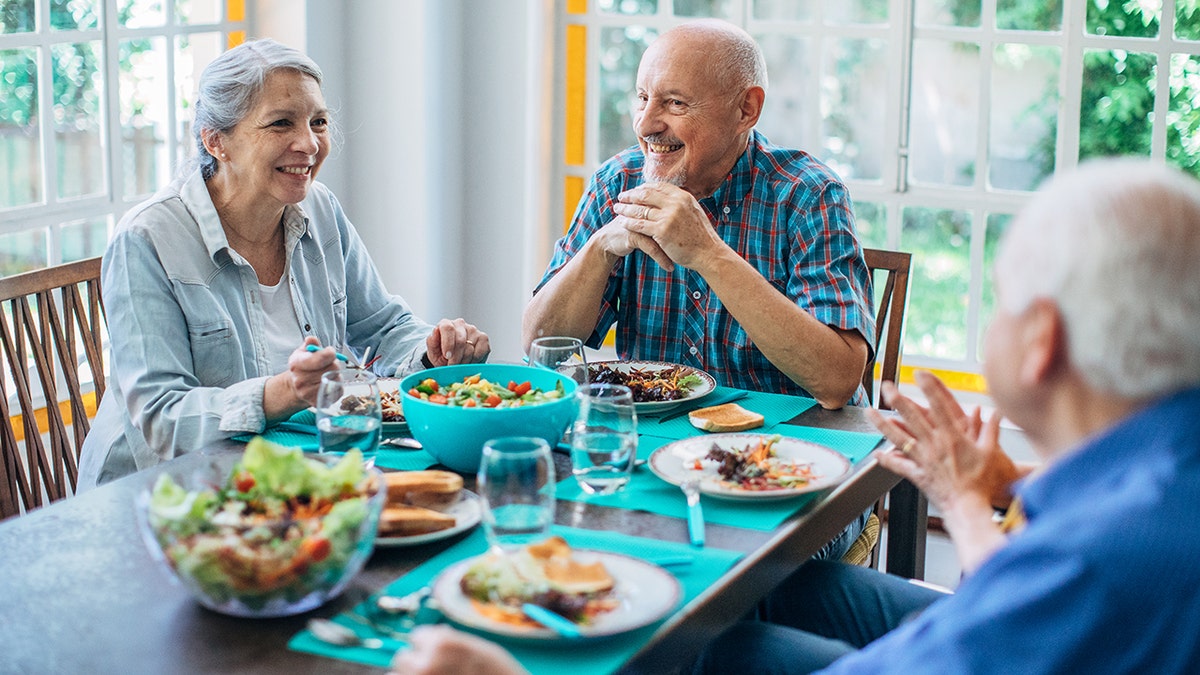 Senior woman and two senior men eating healthy foods and chatting at a table