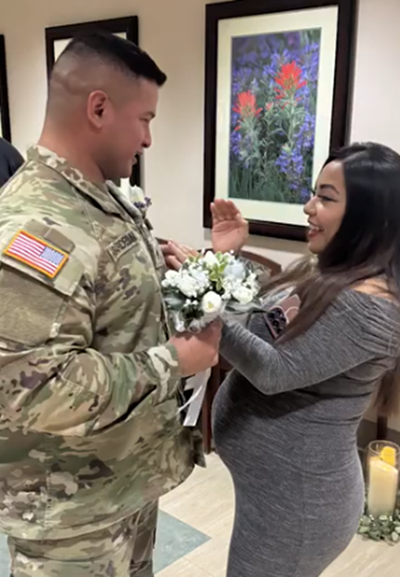 Gian, wearing a military uniform, places a ring on Vanessa's finger while holding a bouquet during a small indoor ceremony