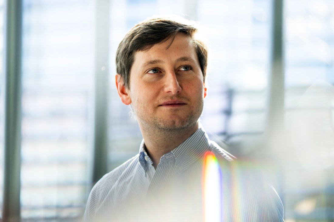 Professor Joshua Curtiss poses for a portrait in front of a brightly lit background.