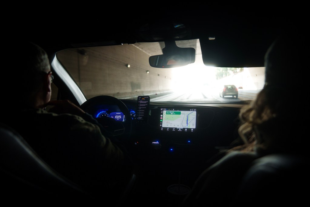 View from the back seat of a car driving through a tunnel, with a driver and passenger silhouetted and the bright exit ahead.