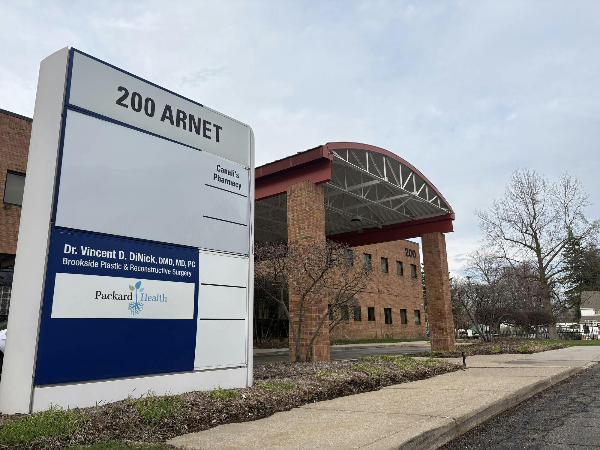 Large outdoor sign for Packard Health features the names of several doctors and the location's address. The brown brick Packard Health building stands in the background.