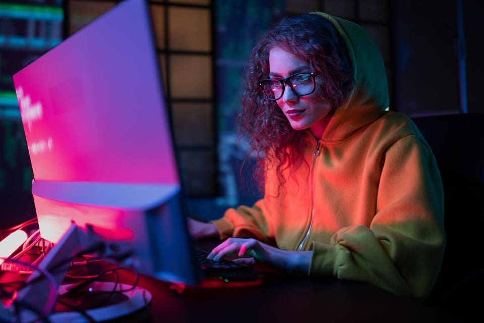 Young hacker woman working on computer at dark place.