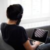 A man with his back to the camera uses a laptop and wears headphones. 