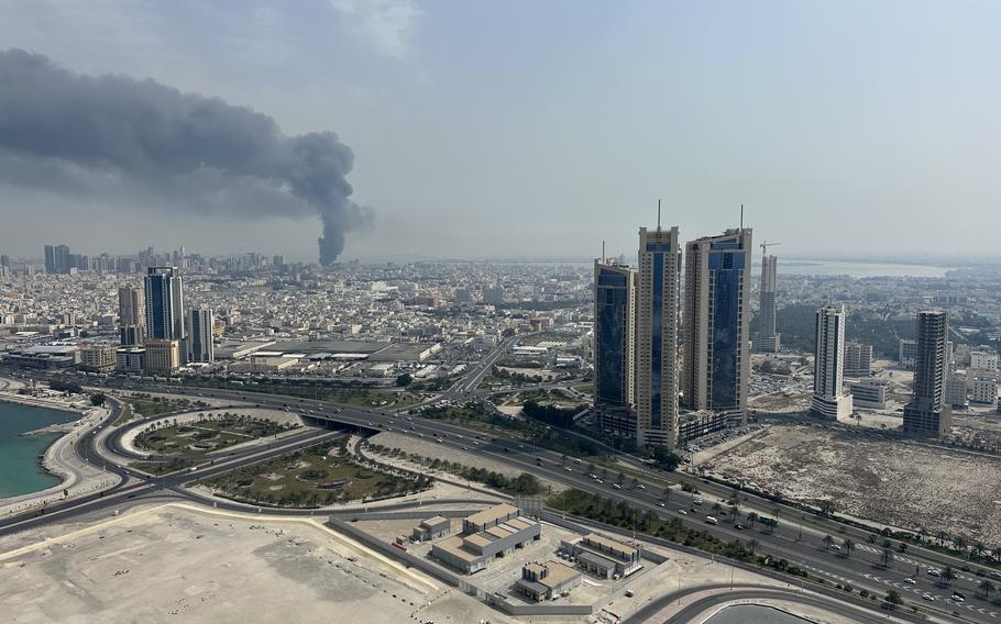A column of black smoke rises over the skyline.