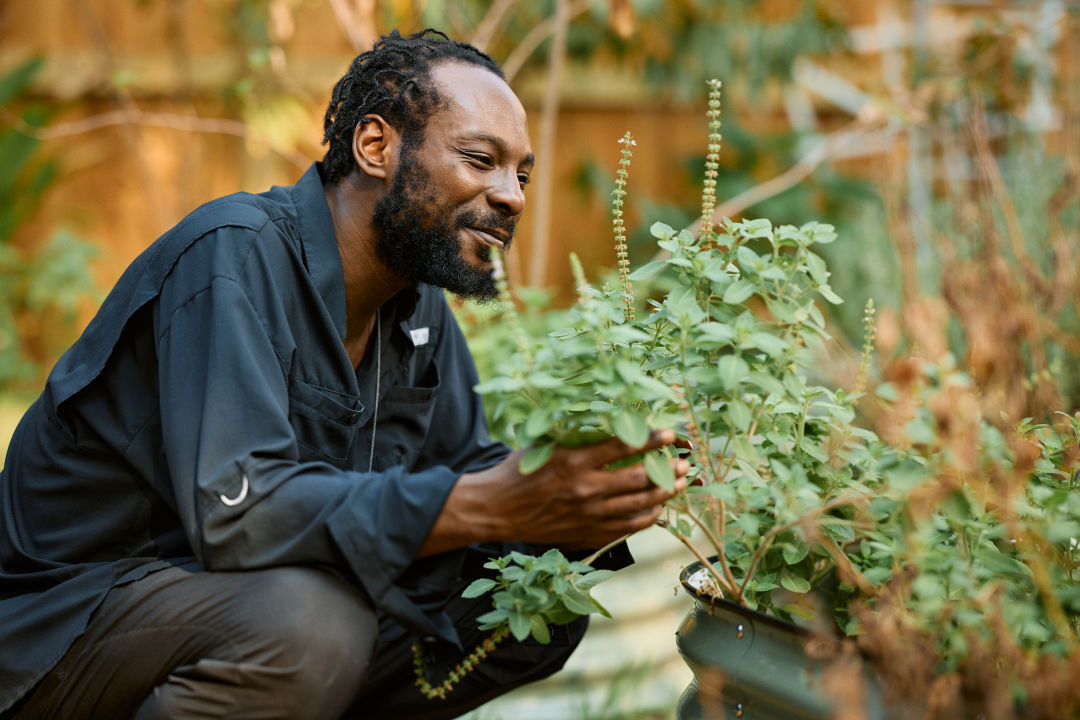 A smiling man kneeling before plants.