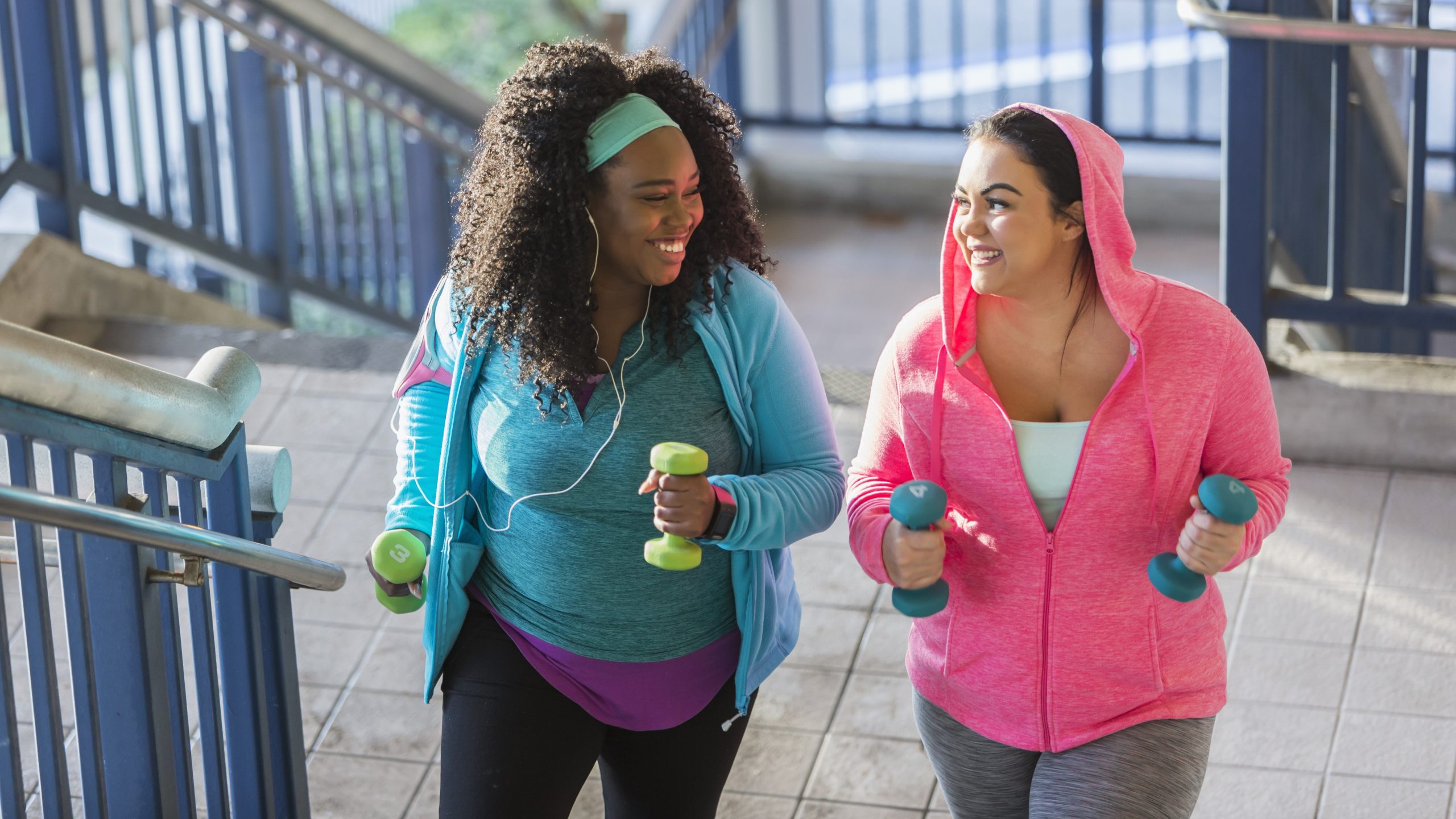 Two women holding weights and walking up stairs