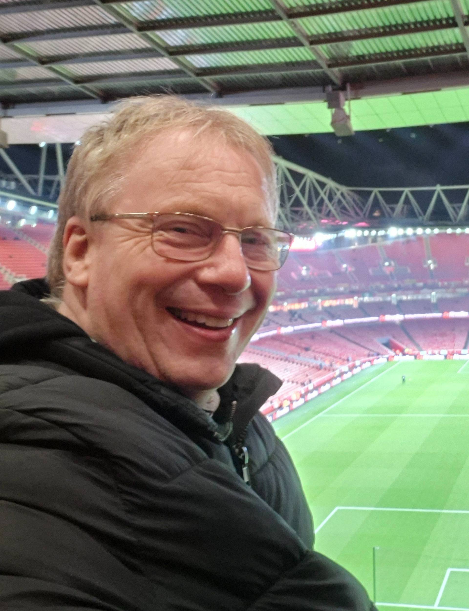 Smiling man in glasses sitting at a football stadium