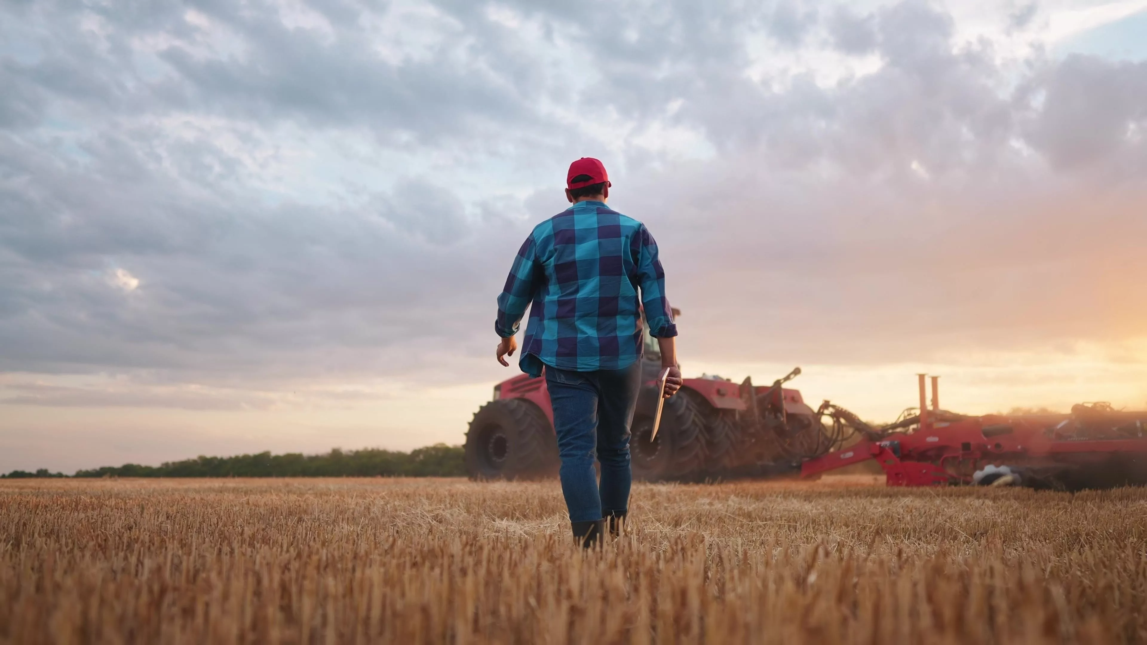 agriculture-farmer-walk-works-in-a-field-next-to-a-tractor-that-plows-the-land-business-agriculture-concept-farmer-with-tablet-works-in-a-field-next-to-a-tractor-at-farm-sunset-mowed-wheat-plows