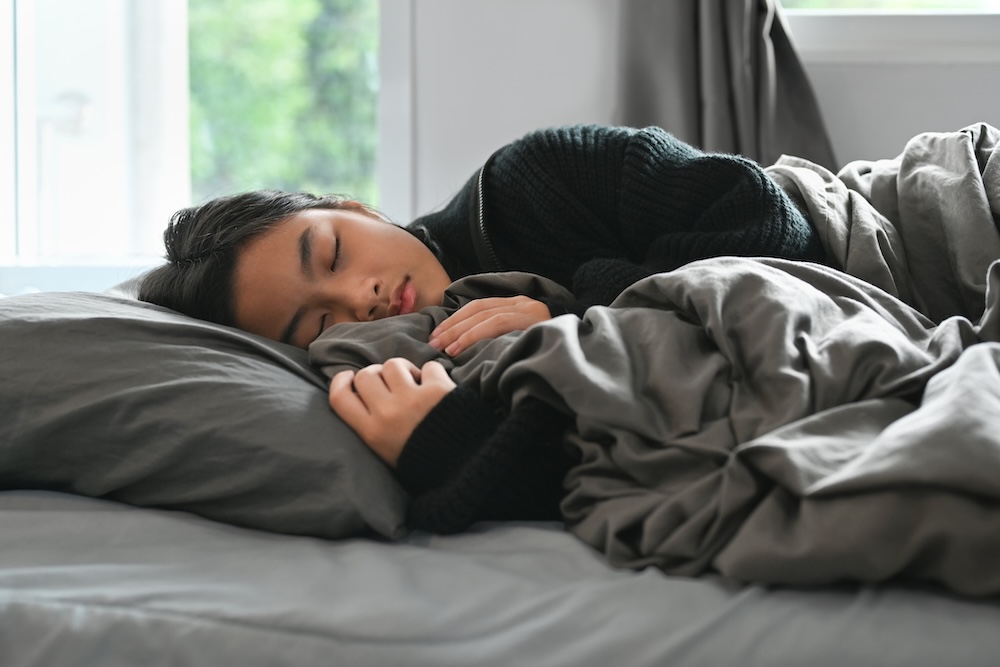 Teenager sleeping in a bed with grey sheets