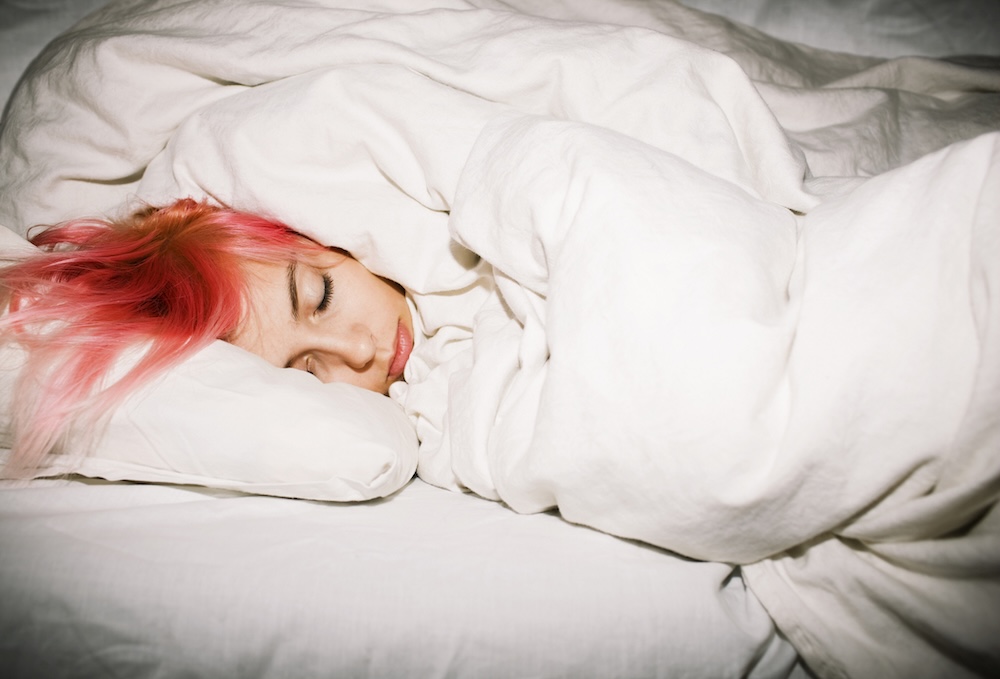 Teenager with pink hair sleeping under white bed covers