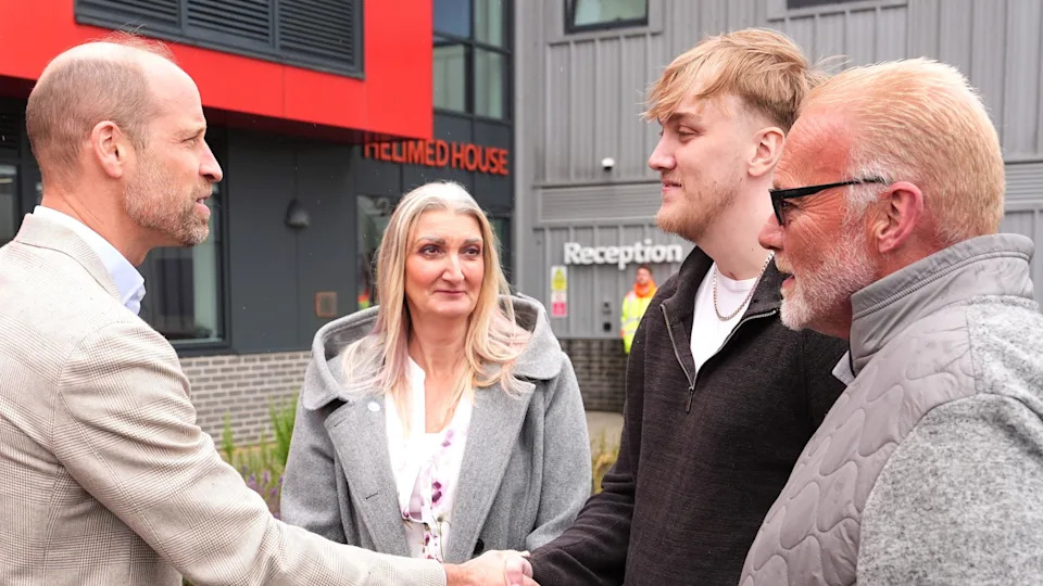 Prince William shakes the hand of a man with blond hair, a beard and wearing a black zip-up top and white-shirt. Looking on are a woman with long blonde hair and a man with short blond hair, sunglasses and a beard. Both are wearing black grey jackets. 