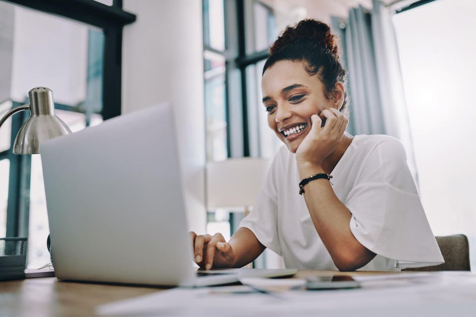 Woman smiling with hand on chin in front of laptop