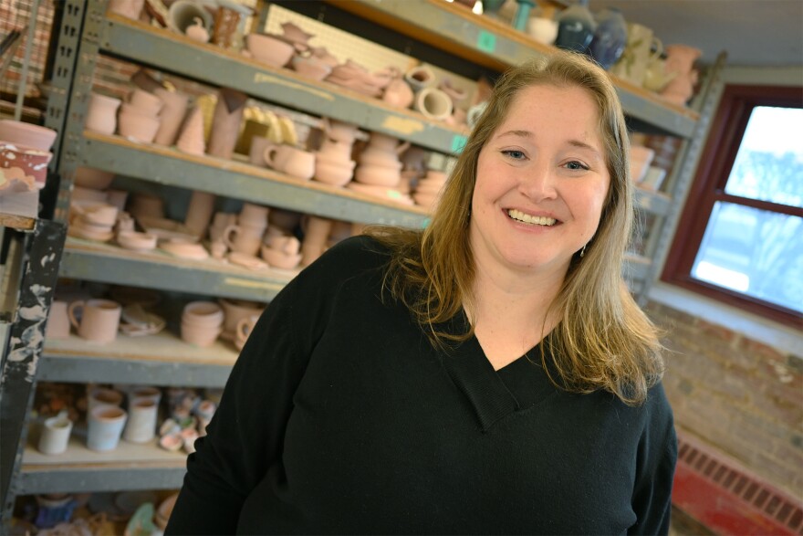 A woman smiles in front of shelves of pottery