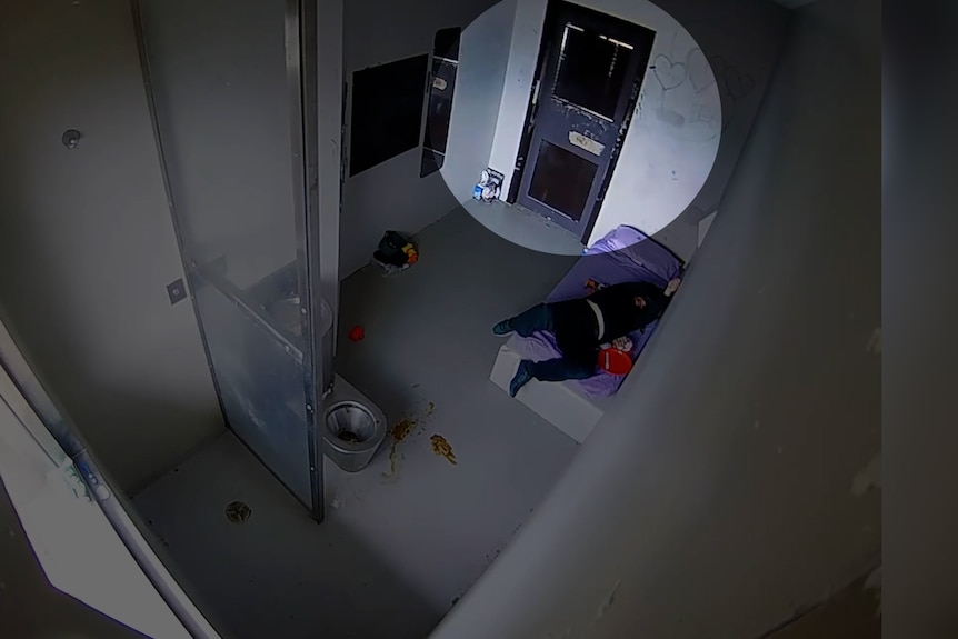 A shadow is seen between the blinds outside the jail cell door window.