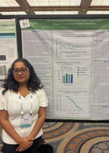 A student stands in front of a research poster at a professional conference