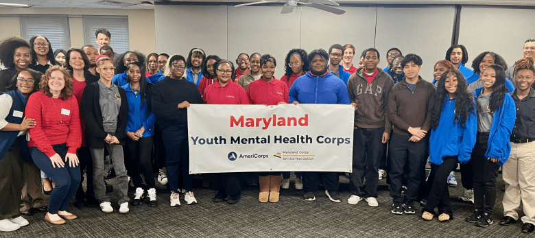 Large group of people holding banner and smiling, banner reads "Maryland Youth Mental Health Corps"