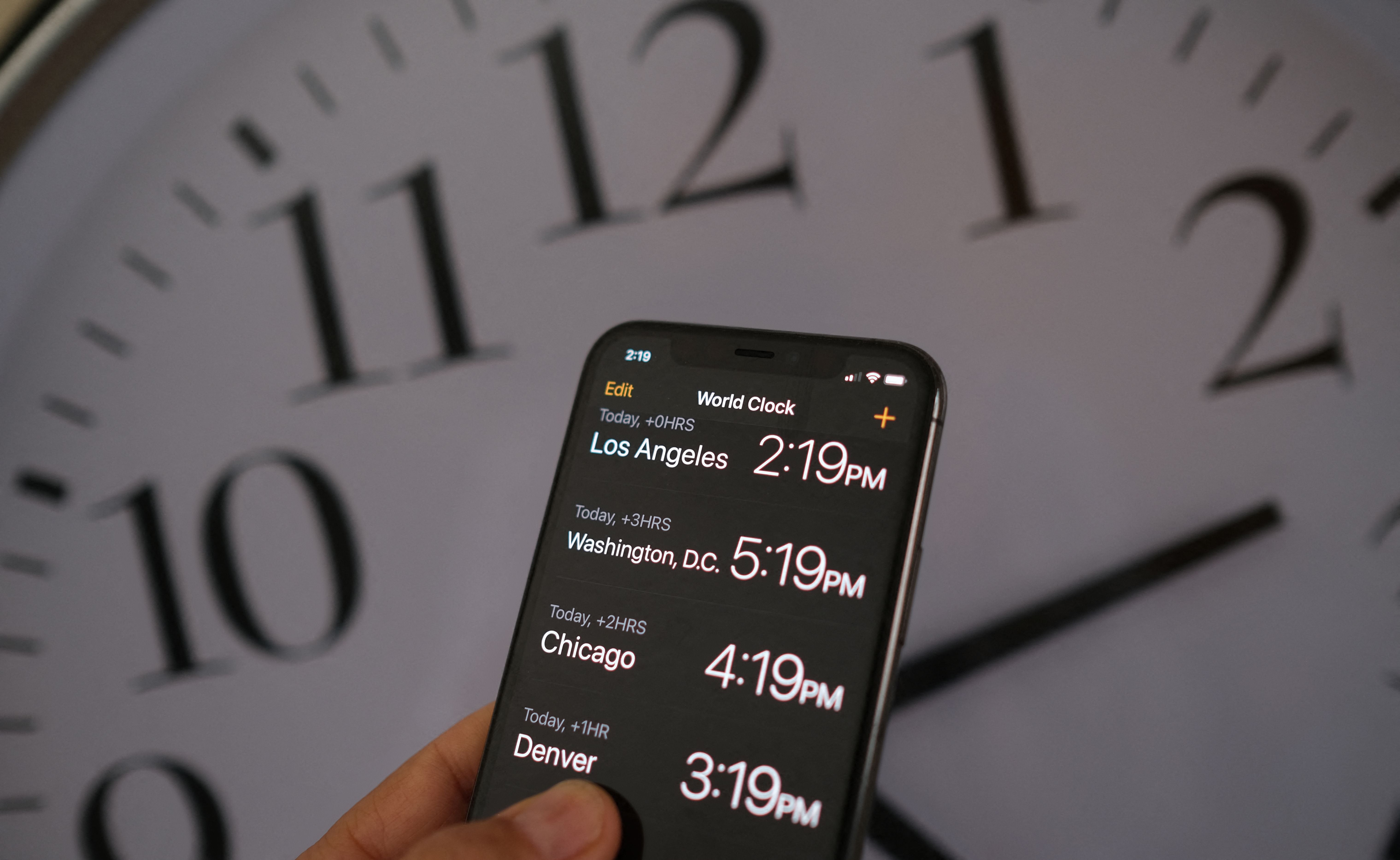 A smartphone showing the time is pictured in front of a clock after the start of daylight saving time