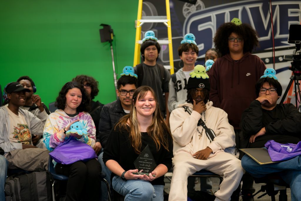 Teacher Lydia Lane poses with Film and Broadcasting students in front of a green screen classroom set.