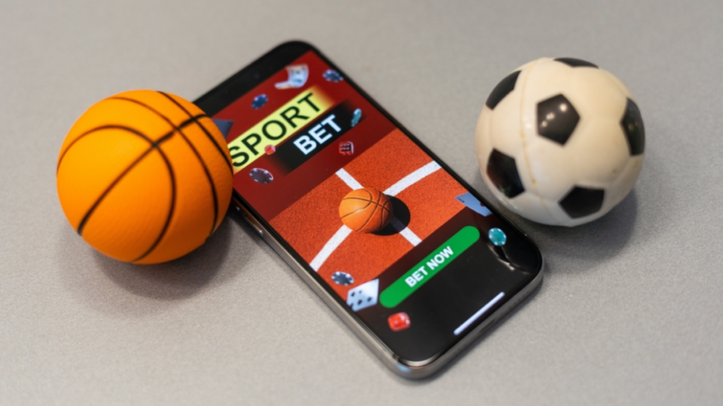 A phone with the words "Sport Bet" on the screen sits on a table next to a small toy basketball and soccer ball.