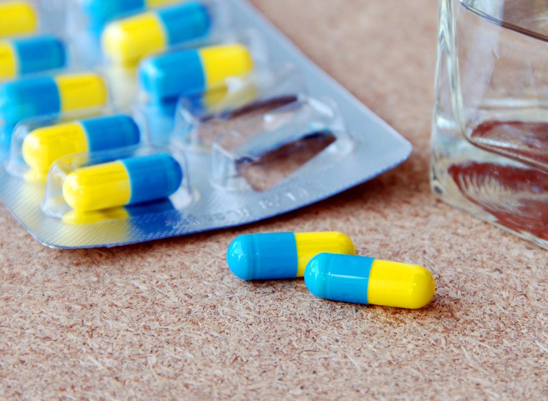 Blue and yellow capsules in blister pack next to glass of water