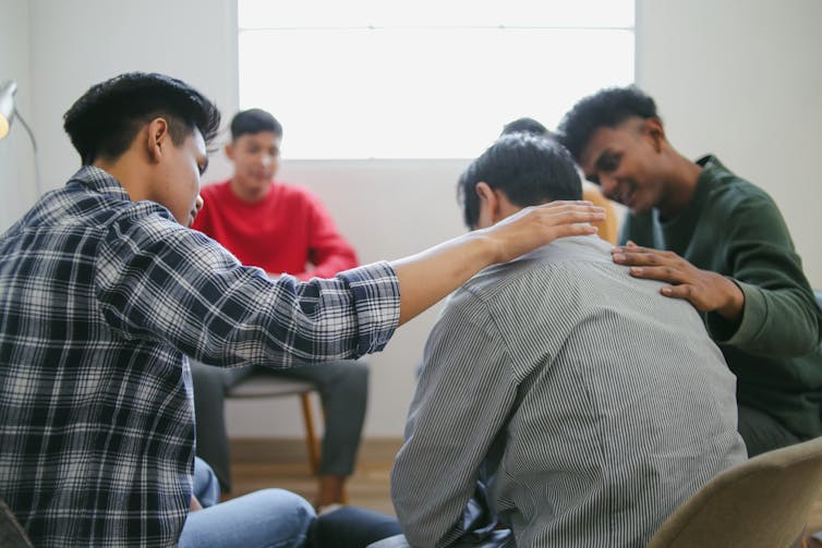 A group of young men sitting in a circle talking, one comforting another
