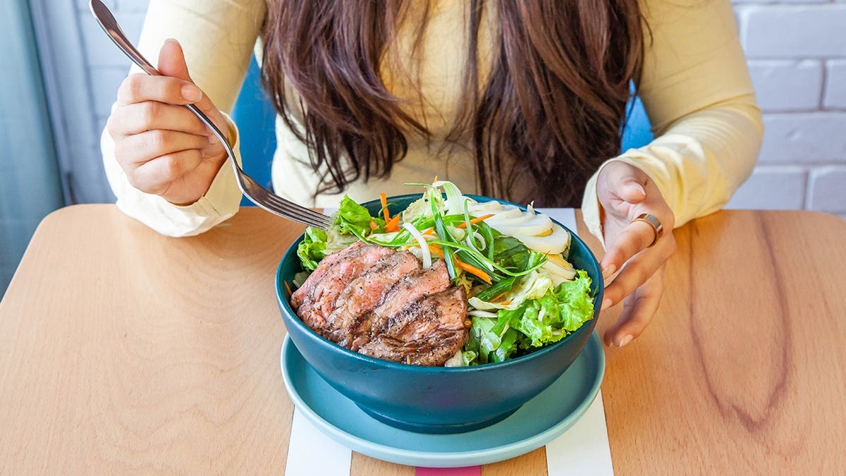 Girl wearing yellow clothes eating a steak and mixed green salad in a cafe.