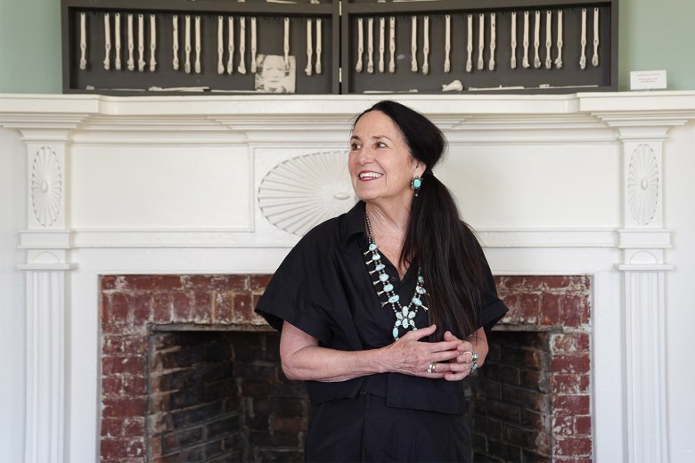 The artist Kimberly Chapman stands in front of a fireplace. Above the fireplace hangs one of her art works, "As Distinctive As You Are."
