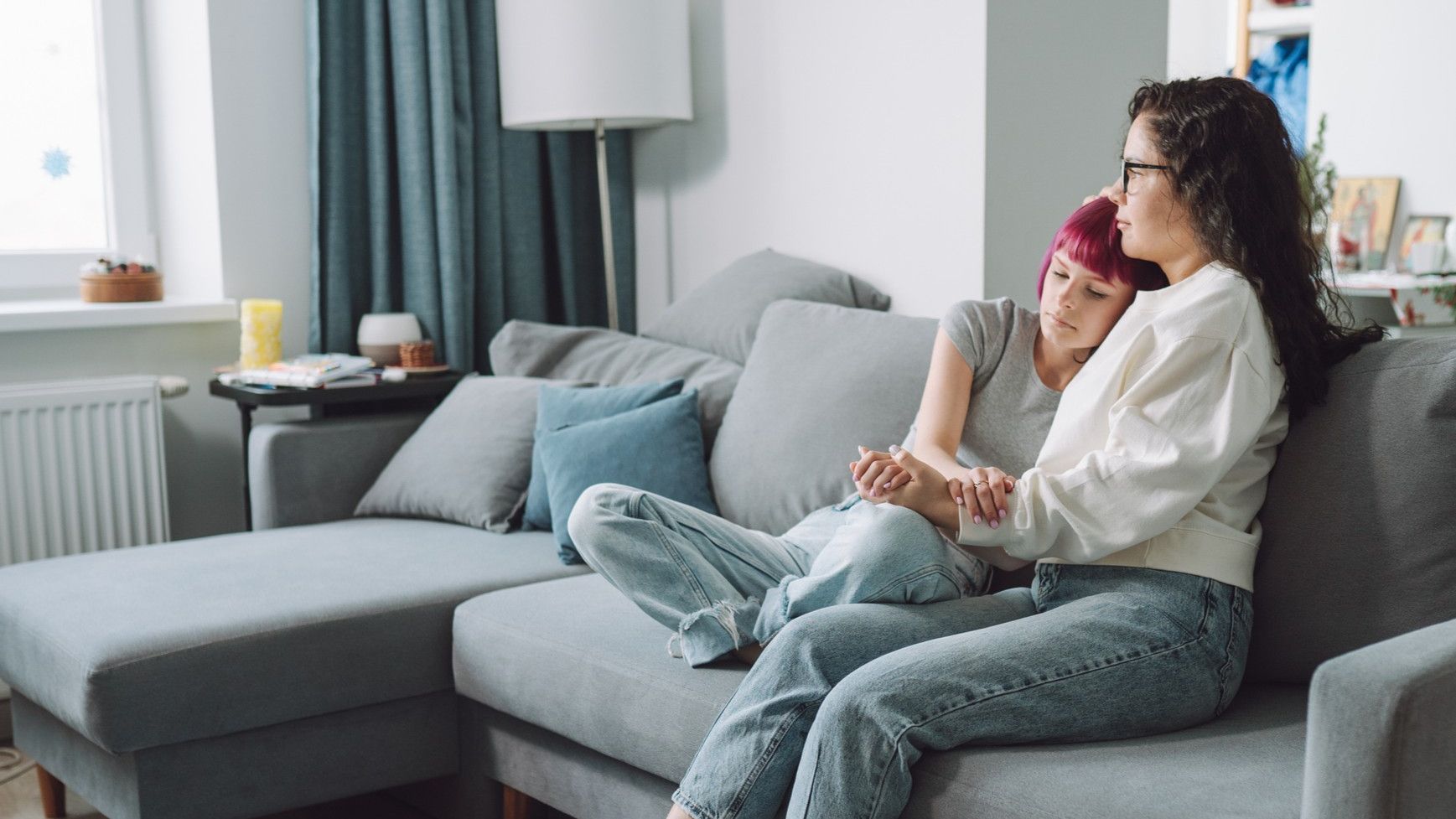 A mom holds her teen daughter sitting on a couch.