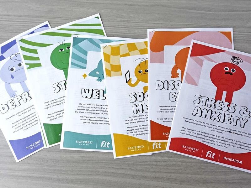 Six sheets of paper on a table outline chapters in a teen mental health workbook.