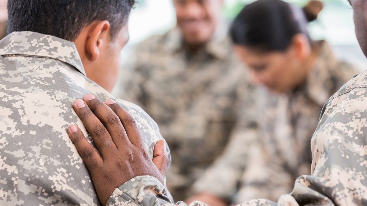 Unrecognizable soldier placing hand on fellow soldier during support group meeting