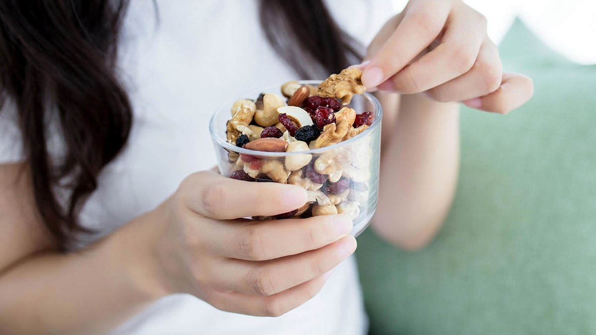 A woman eating nuts and dried fruits from a glass jar.
